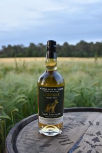 Whiskey bottle on a wooden barrel outdoors in a grassy field with trees in the distance.