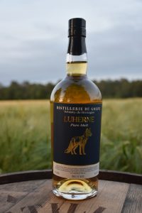 Close-up of a whiskey bottle with a black cap, outdoors on a wooden table, label reads 'LUHERNE' with a dog illustration.